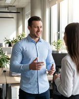Man in a light blue button-down talking with a colleague at the office, the V-Frame Padded Undershirt underneath